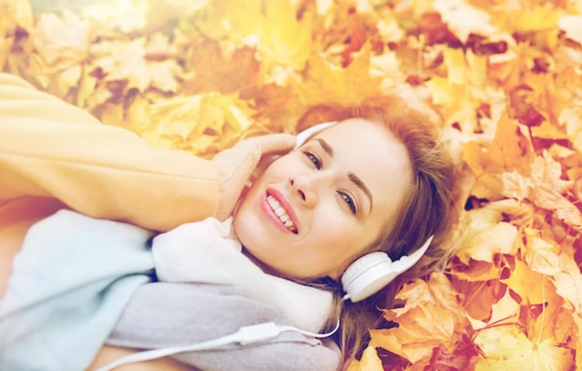 person listening with headphones autumn leaves